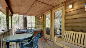 A wooden deck with a table and chairs, a hot tub, and a door with blinds. - Bavarian Hideaway 24 (Sautee Nacoochee)