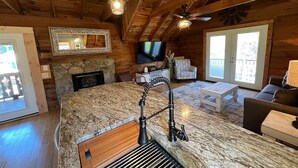 A kitchen with a granite countertop, a wooden backsplash, and a stone fireplace. There is a television mounted on the wall and a ceiling fan. - Bavarian Brook Condo 14 (Helen)