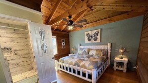 A bedroom with a wooden ceiling, a bed with a patterned bedspread, a small bedside table, and a wall-mounted ceiling fan. - Bavarian Brook Condo 14 (Helen)