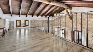 Une pièce spacieuse avec un plafond haut, des poutres en bois, un balcon doté d’une rambarde en métal et un mur en pierre.
