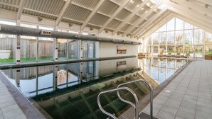 Ein Hallenbad mit großen Glaswänden, gefliestem Boden und einer Metallhandläufe.