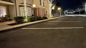 Une vue nocturne d’une rue bordée de maisons, avec un parking et des lampadaires.