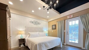 Une chambre d’hôtel avec un grand lit, un lustre, une table de chevet avec une lampe, une porte avec un panneau indiquant la sortie et une fenêtre avec des rideaux.