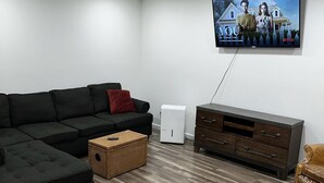 Ein modernes Wohnzimmer mit einem Ecksofa, einem flachbildfernseher an der Wand, einem weißen Luftreiniger und Holzboden.
