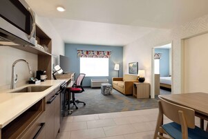 Una habitación de hotel compacta con kitchenette, un sofá, una pequeña mesa y una cama.