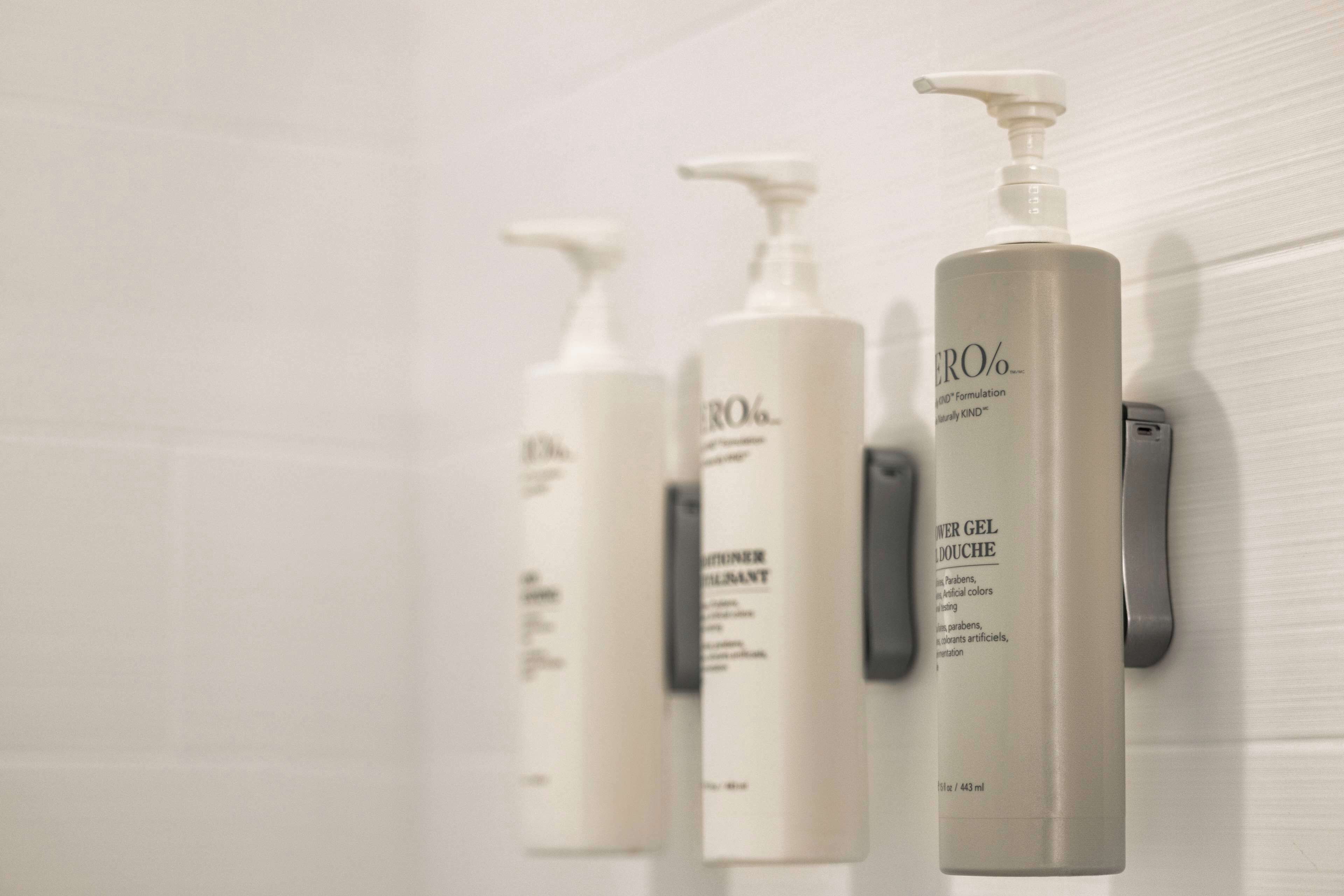 Three white bottles of skincare products on a wall.