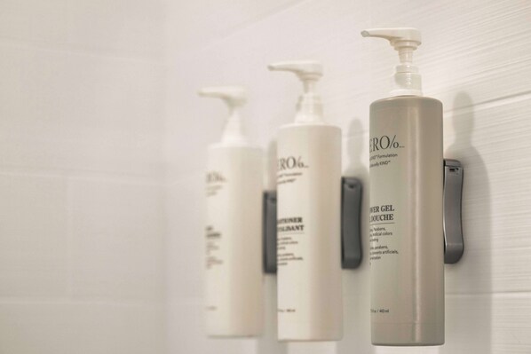 Three white bottles of skincare products on a wall. - Home2 Suites by Hilton Livingston Yellowstone (Livingston)