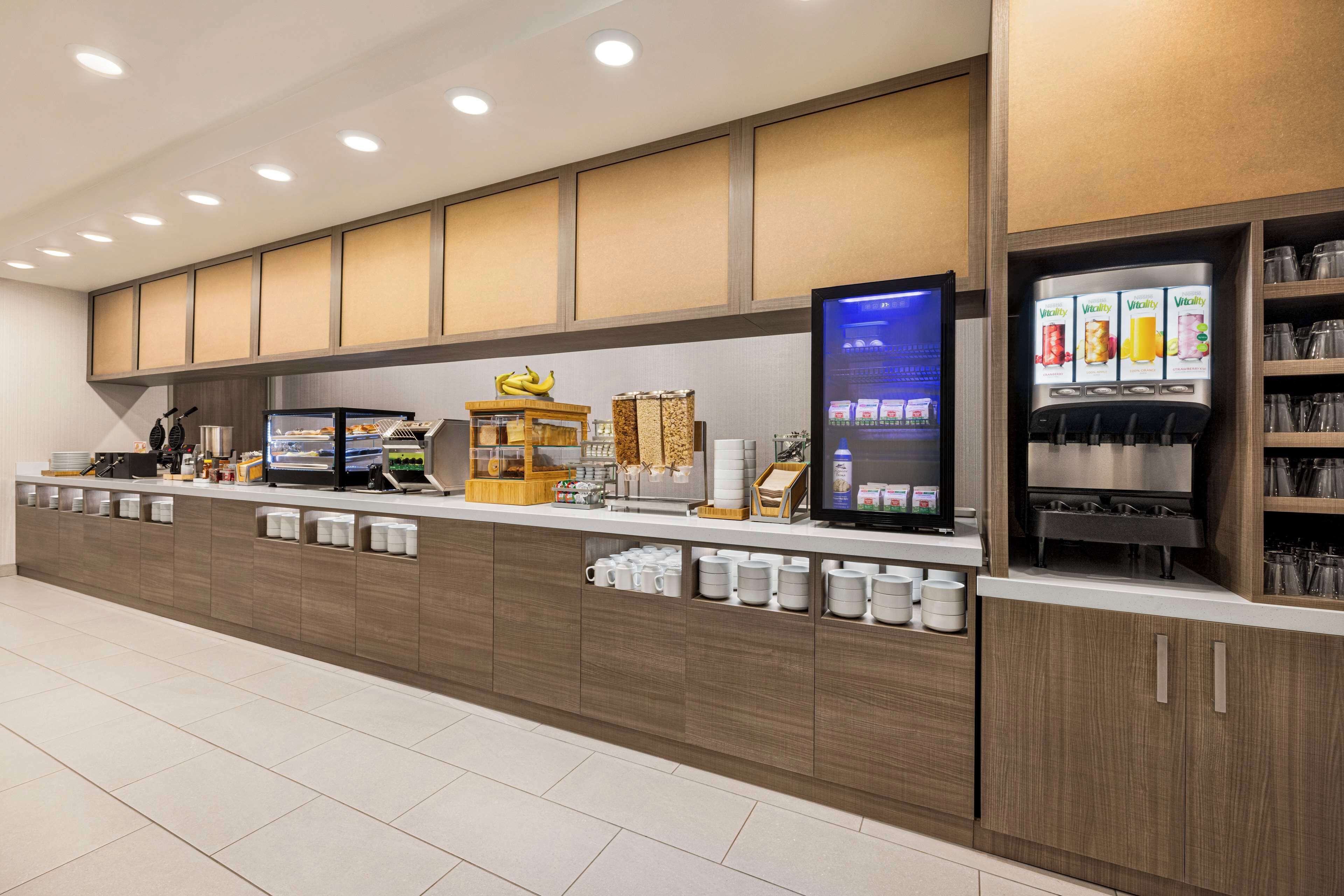 Una barra de desayuno moderna con una máquina de café, una presentación de frutas y un dispensador de bebidas.