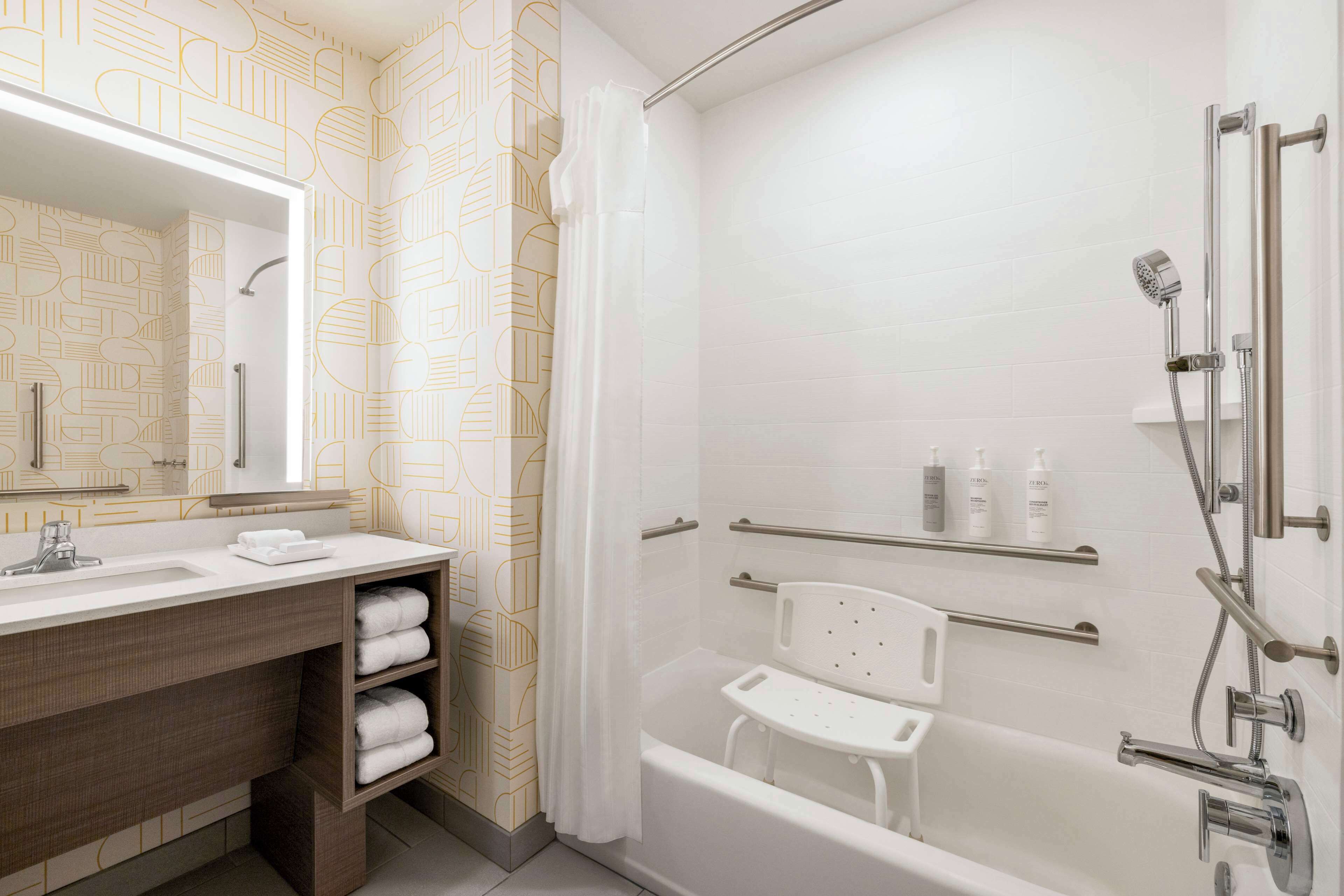 A modern bathroom with a large mirror, a bathtub, a shower area, and a vanity with towels.