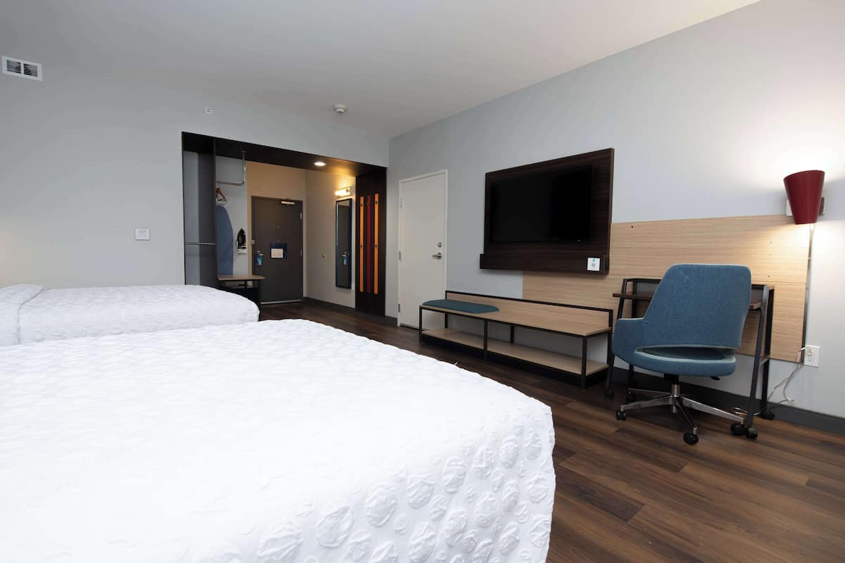 A hotel room with two beds, a desk, a chair, a TV, and a red lamp.