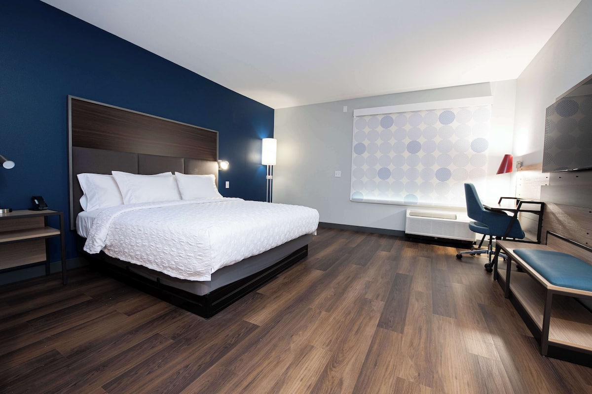 A hotel room with a bed, a desk, a chair, and a window with patterned curtains.