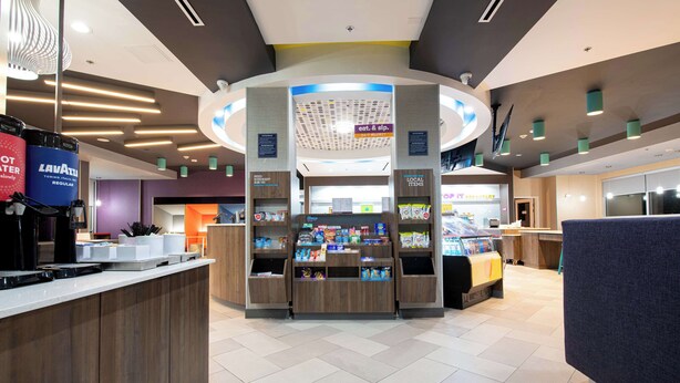 A modern retail area with a central kiosk, various product displays, and a coffee station. - Tru By Hilton Lewisville Vista Ridge Mall (Lewisville)