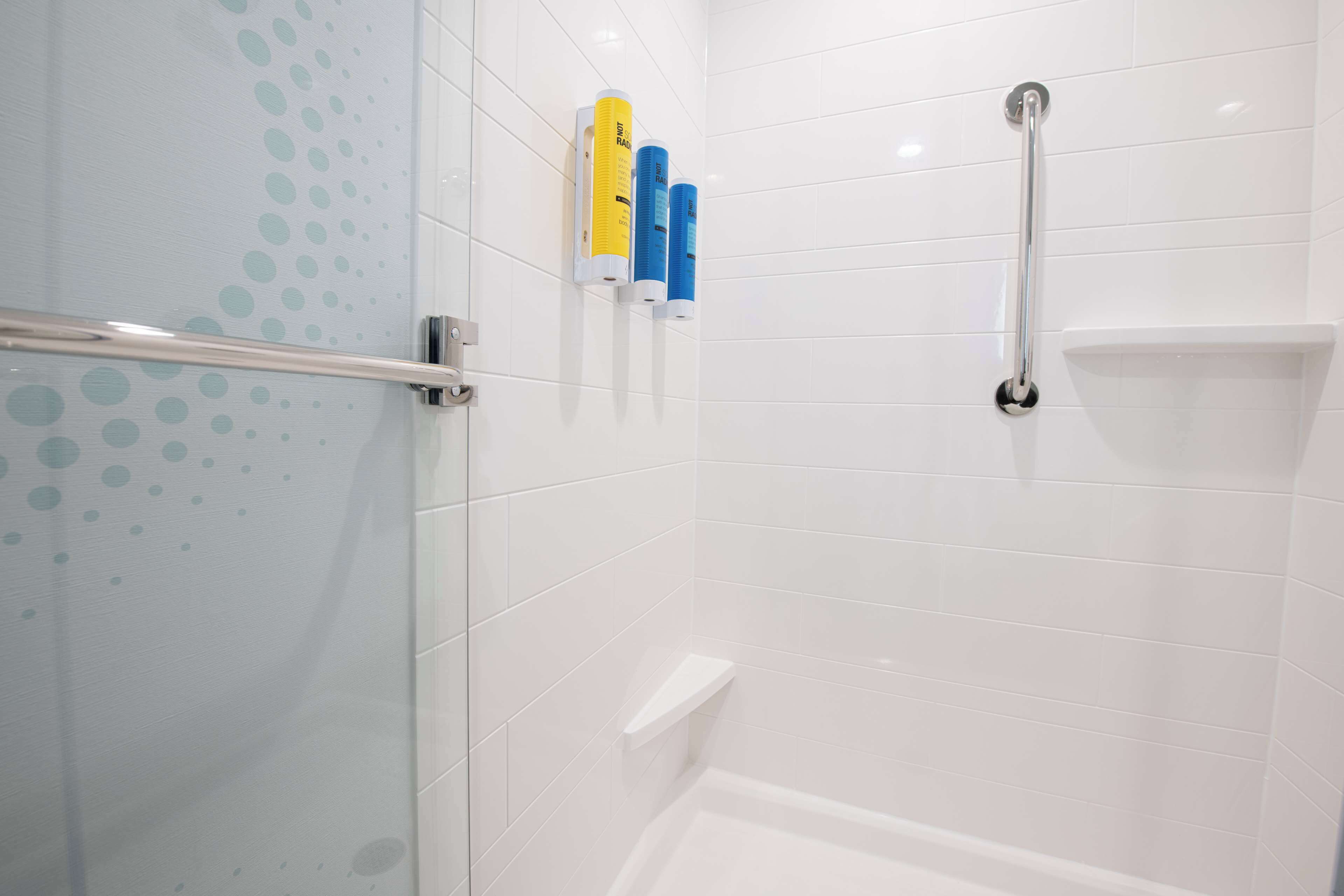 A bathroom with white tiled walls, a glass shower enclosure, and a handrail.