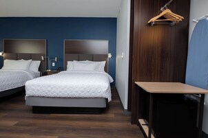 Habitación de hotel con dos camas, un escritorio, una silla y un perchero de madera.
