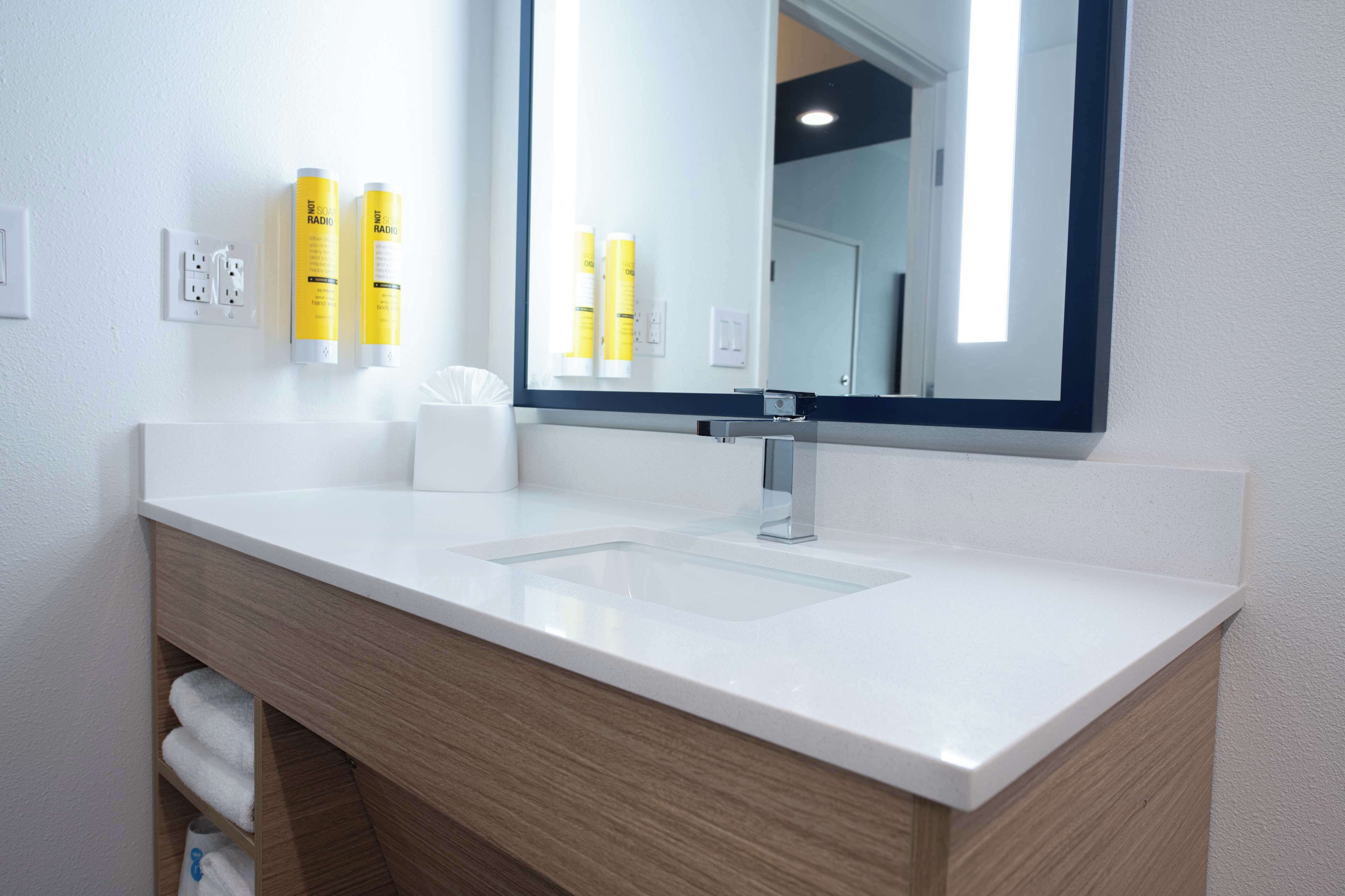 Un baño moderno con un lavamanos blanco, tocador de madera y un espejo grande.