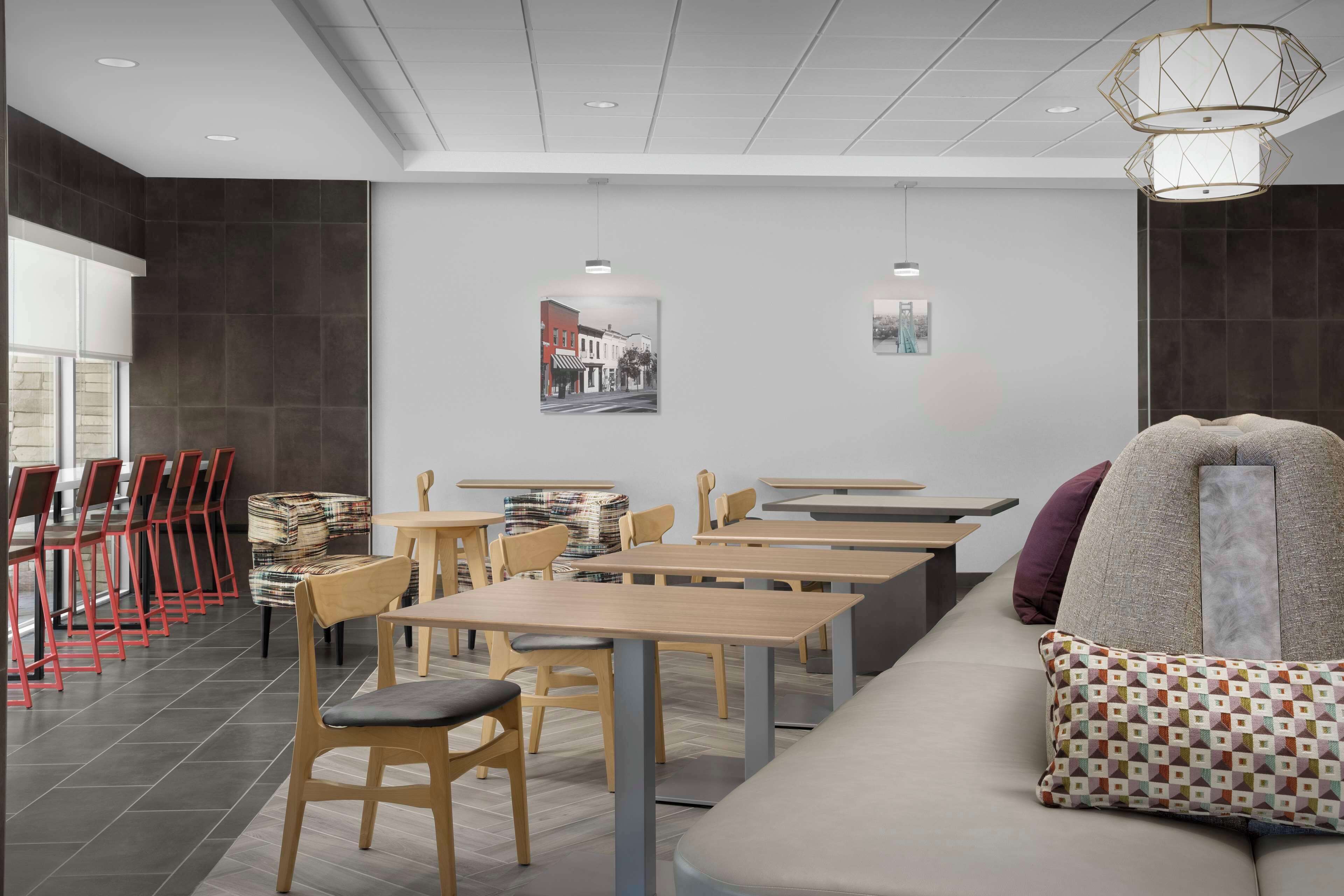 A modern dining area with wooden tables and chairs, a sofa with patterned cushions, and artwork on the walls.