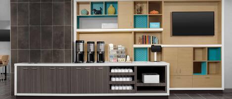 A modern kitchen with dark cabinetry, a built-in coffee station, and a flat-screen TV mounted on the wall.