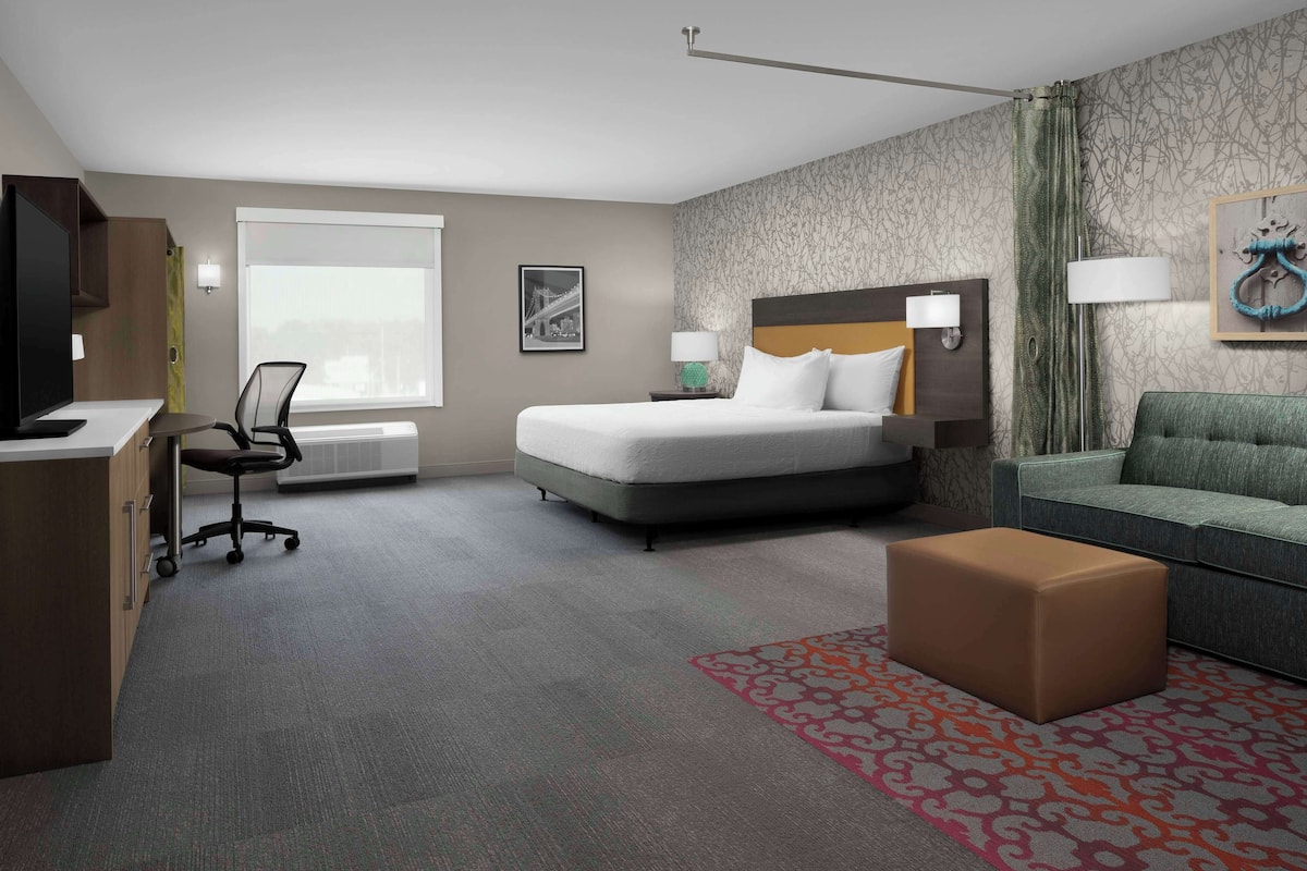 A hotel room with a bed, a desk, a chair, a sofa, and a patterned rug.