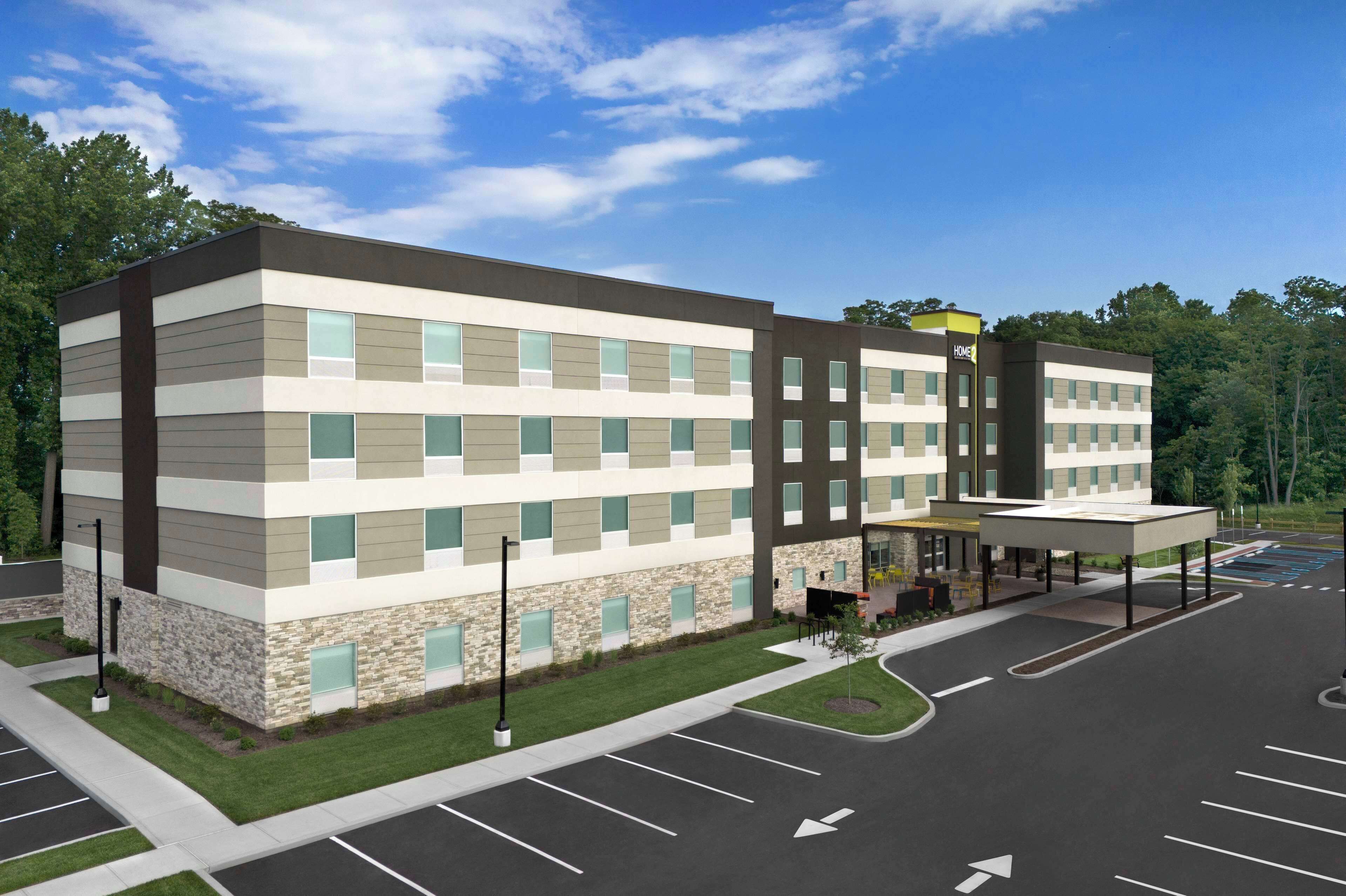 A multi-story hotel with a modern design, featuring a mix of stone and panel exteriors, a covered outdoor seating area, and a parking lot.