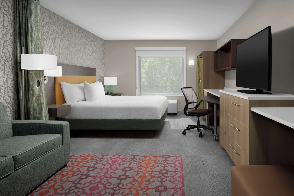 A hotel room with a bed, a desk, a television, a chair, and a sofa.