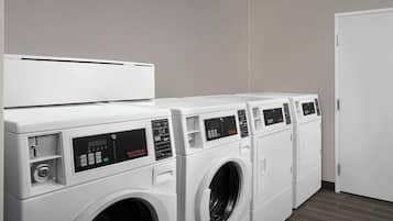 A row of white front-loading washers in a laundry room with a plain wall and a door on the right.