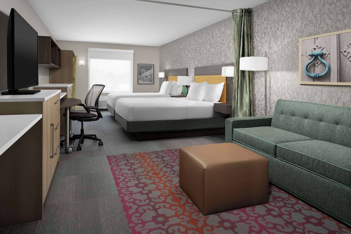 A hotel room with a bed, a desk, a television, a sofa, and a patterned rug.