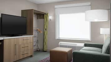 Ein Hotelzimmer mit Flachbildfernseher, einem Holzschrank, einem grünen Sofa, einem gemusterten Teppich und einem großen Fenster mit weißem Vorhang.