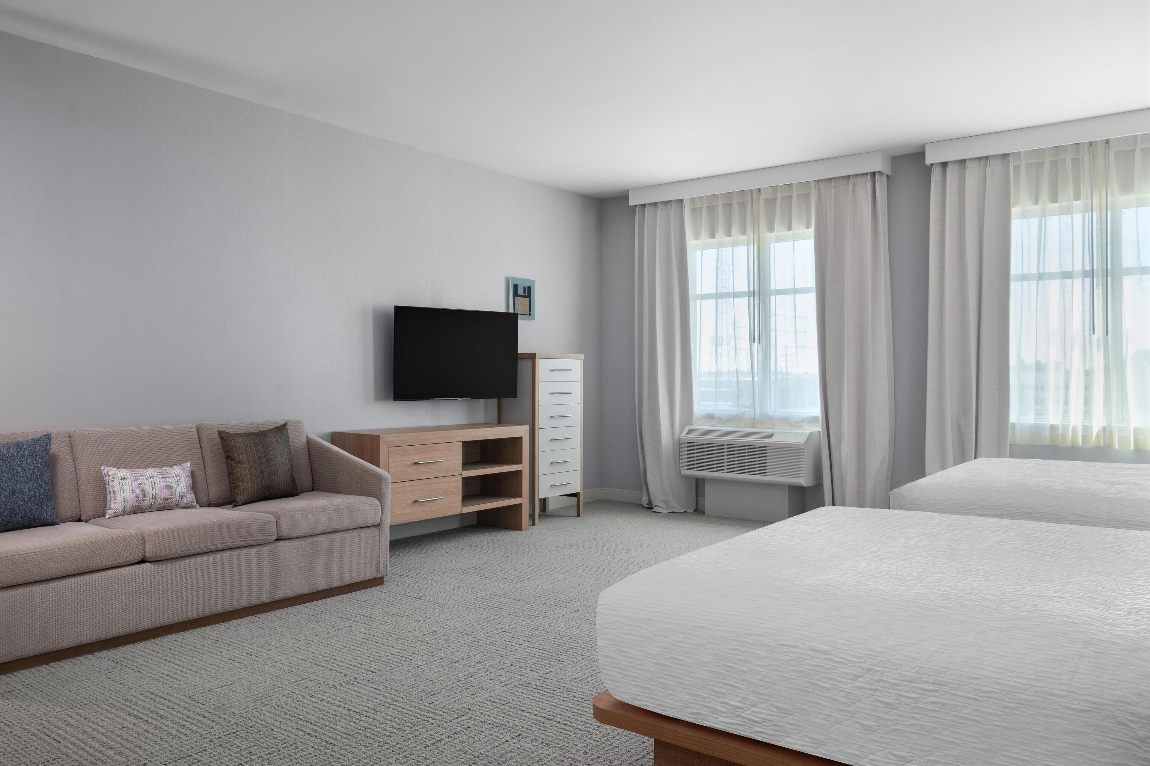 A hotel room with a bed, a sofa, a TV, a dresser, and a window with curtains.