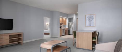 A modern living room with a minimalist design, a flat-screen TV, a wooden coffee table, a sofa, and a dining area with a small table and chairs.