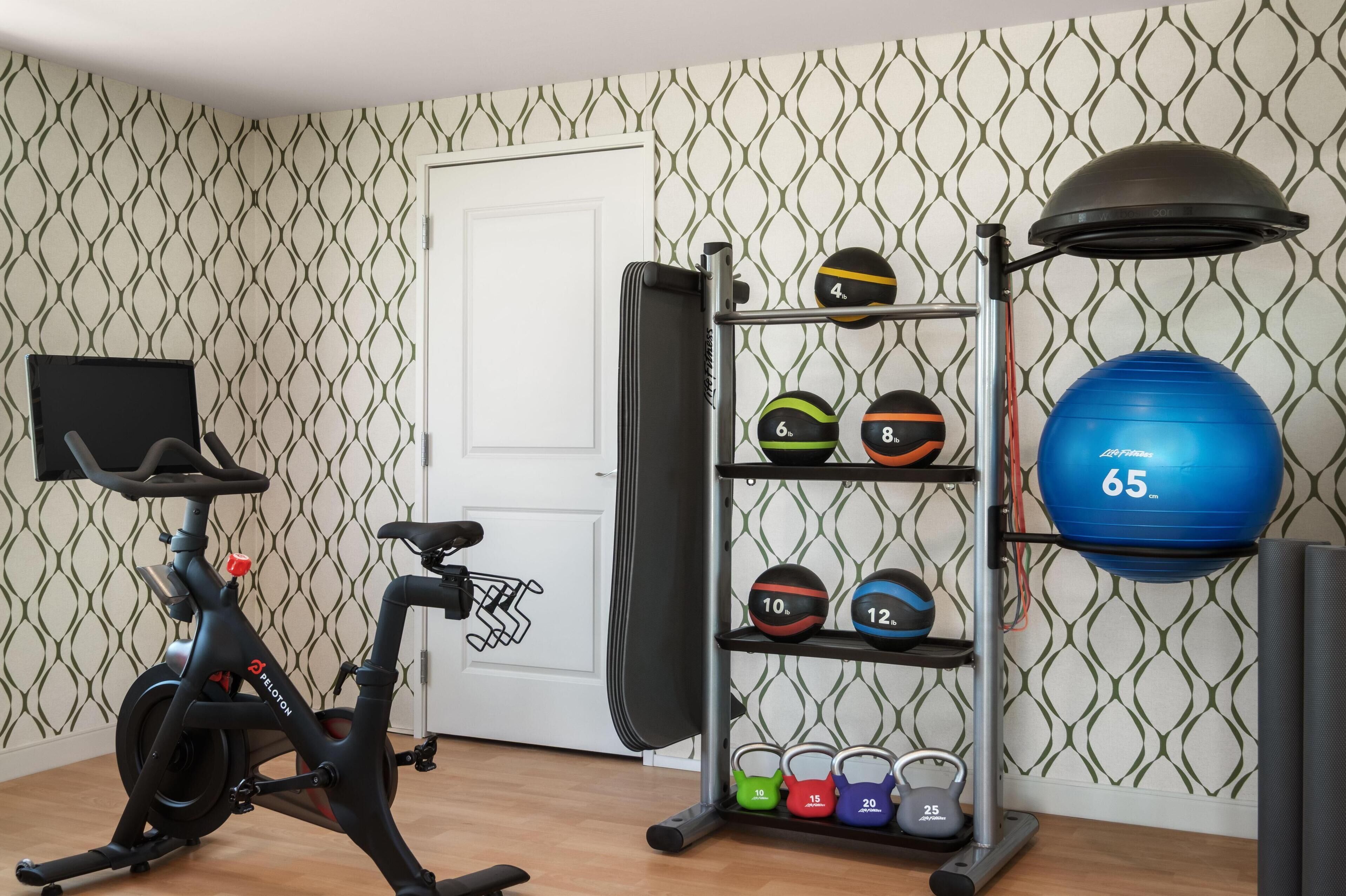 A home gym with an exercise bike, a weight rack with various weights, and a large blue exercise ball.