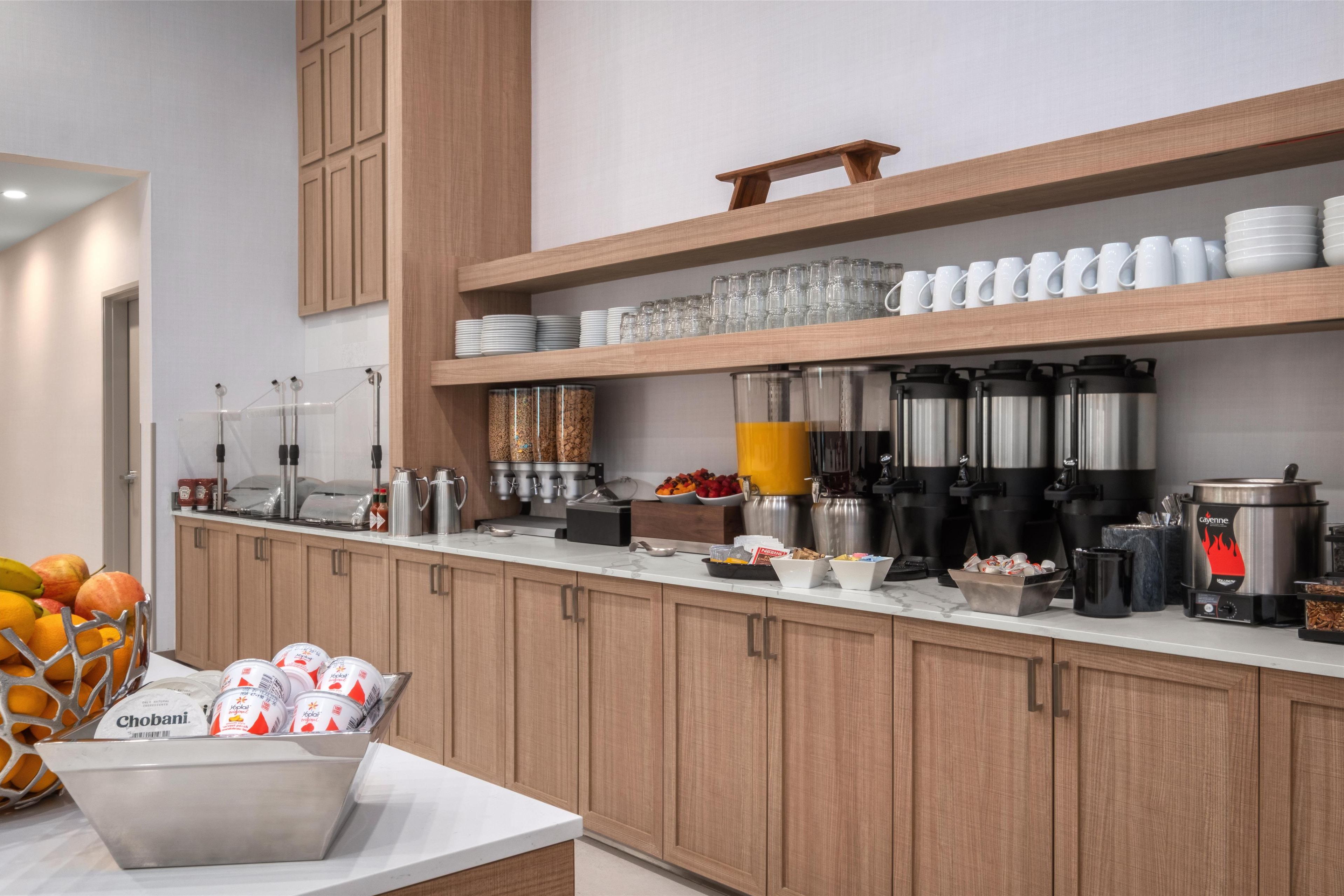 A modern kitchen with wooden cabinets, stainless steel appliances, and a variety of food items and utensils on the counter.