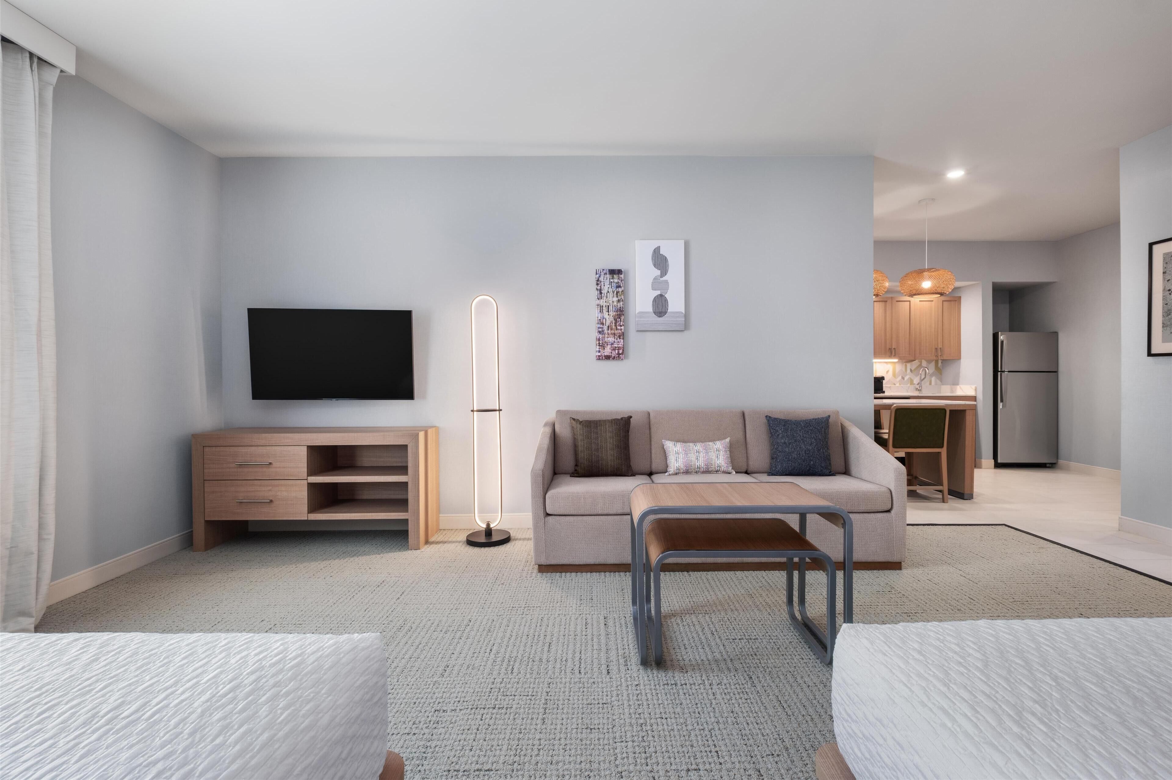 A modern living room with a sofa, a coffee table, a TV, and a kitchen in the background.