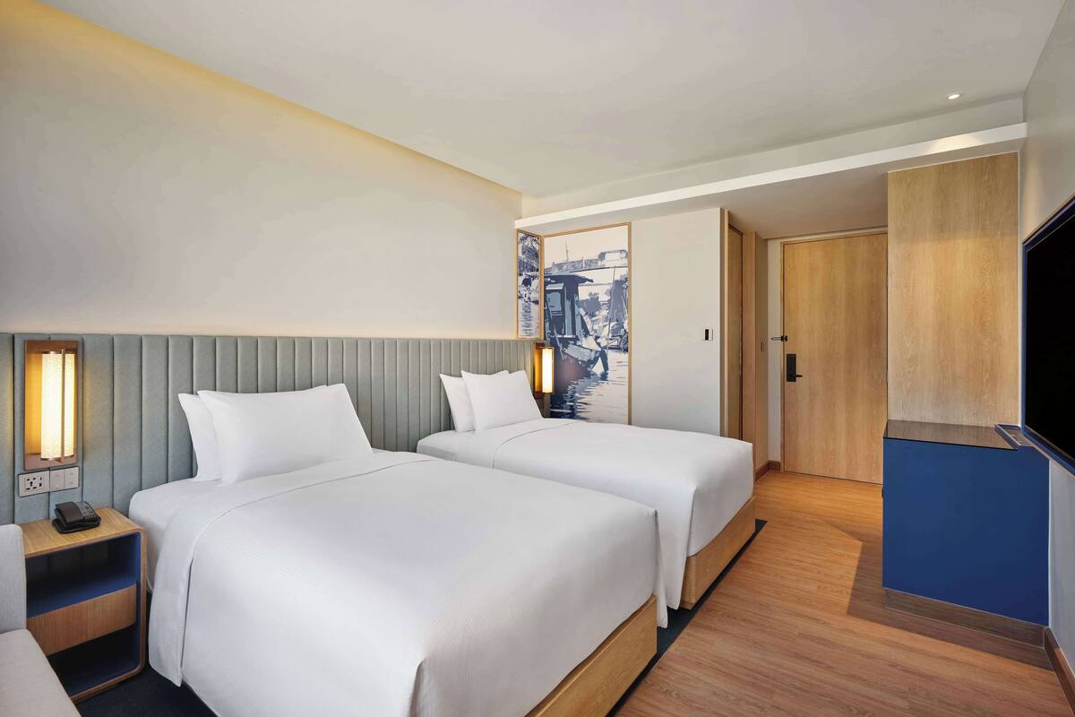 A hotel room with two beds, a wooden floor, a flat-screen TV, and a painting on the wall.