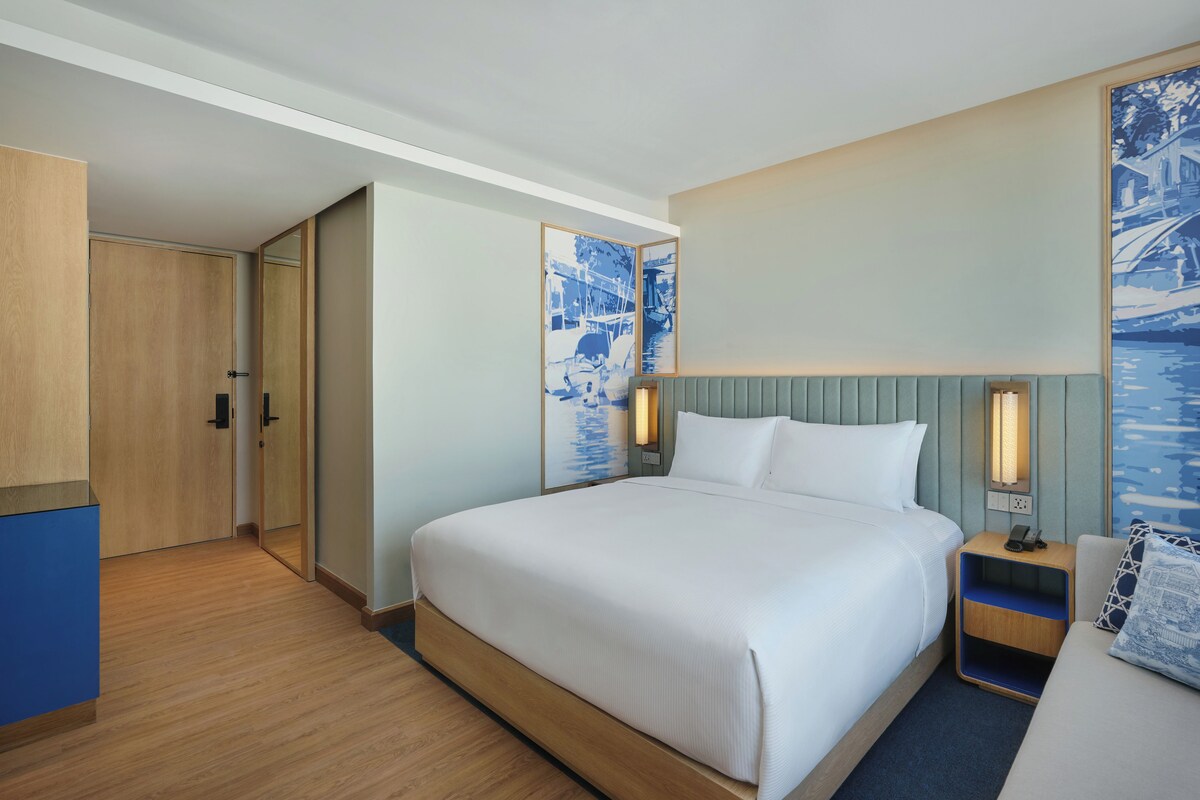 A hotel room with a large bed, bedside tables, a wardrobe, and artwork on the walls.