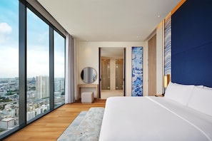 A modern hotel room with a large bed, a view of the city, a bathroom, and a desk area.