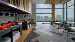 A modern dining area with a high ceiling, large windows, and a city view. - Hilton Garden Inn Bangkok Riverside (Bangkok)