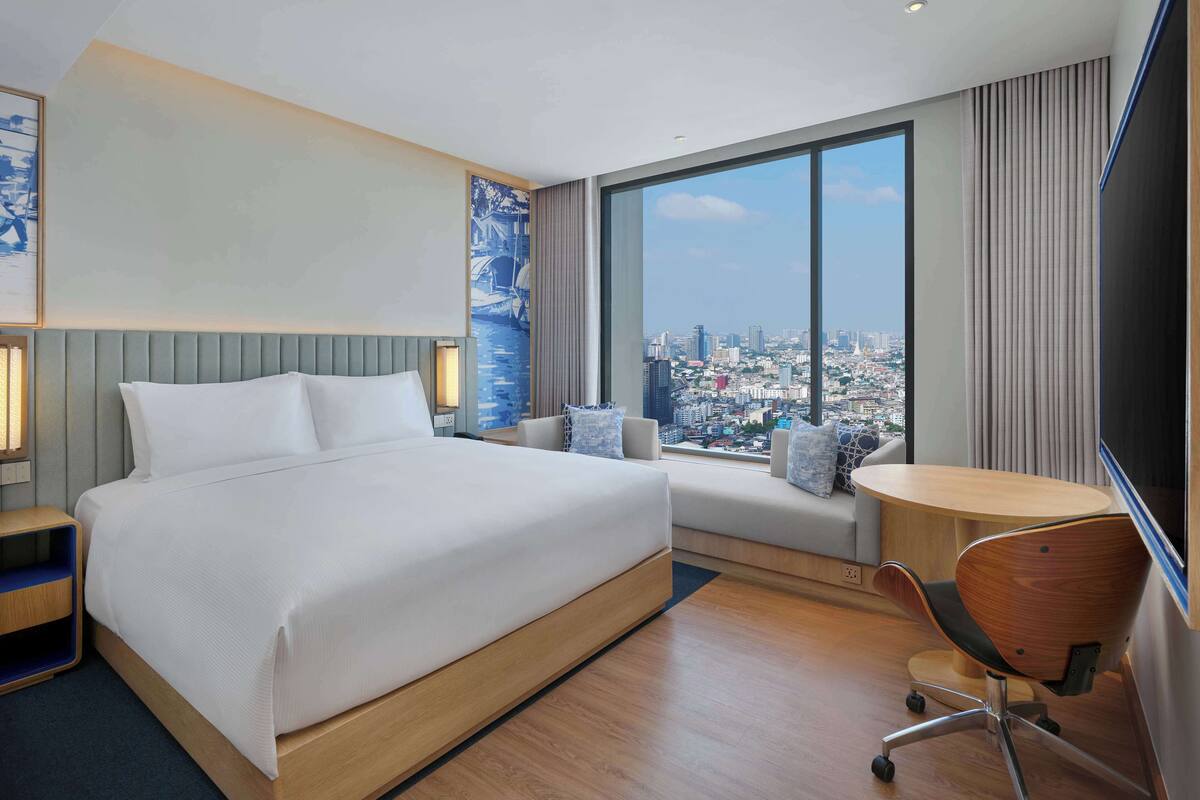 A hotel room with a large bed, a desk, and a view of a cityscape.