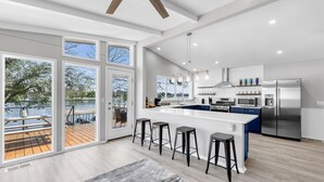 A modern kitchen with a large island, bar stools, and a view of a lake through large windows. - The Blue Haven Getaway in cozy Kingsland, TX (Kingsland)