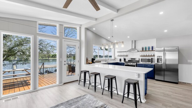 A modern kitchen with a large island, bar stools, and a view of a lake through large windows. - The Blue Haven Getaway in cozy Kingsland, TX (Kingsland)