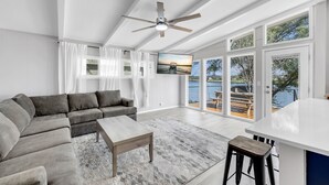 A modern living room with a gray sectional sofa, a wooden coffee table, and a large window offering a view of a lake and dock. - The Blue Haven Getaway in cozy Kingsland, TX (Kingsland)