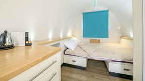 A compact room with a bed, bedside table, and a small kitchenette area.