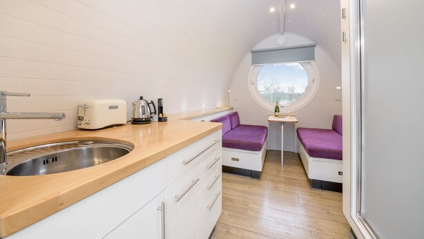 A compact kitchen with a sink, toaster, and kettle, a small dining area with a table and chairs, and a window with a view.