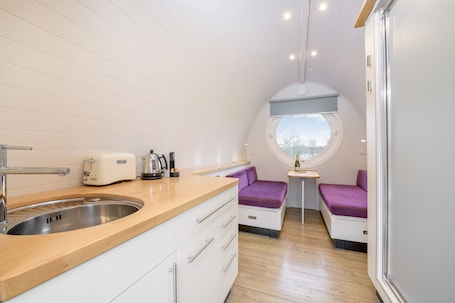 A compact kitchen with a sink, toaster, and kettle, a small dining area with a table and chairs, and a window with a view.