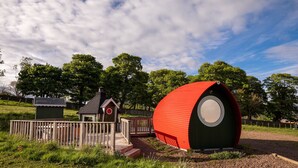 A red spherical structure with a door, a small wooden cabin, and a fenced area with a pathway.
