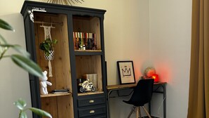 A room with a black wooden cabinet, a desk with a chair, a framed picture, and a plant. - Les Copains D'abord (Nîmes)