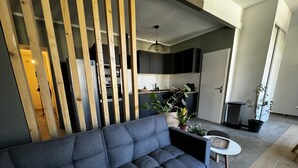 A modern living room with a dark grey sofa, a small round table, and a kitchen area in the background. - Les Copains D'abord (Nîmes)