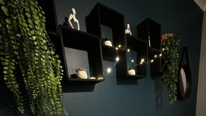 A bedroom with a bed, a bedside table, a mirror, and wall-mounted shelves with decorative items and plants. - Les Copains D'abord (Nîmes)
