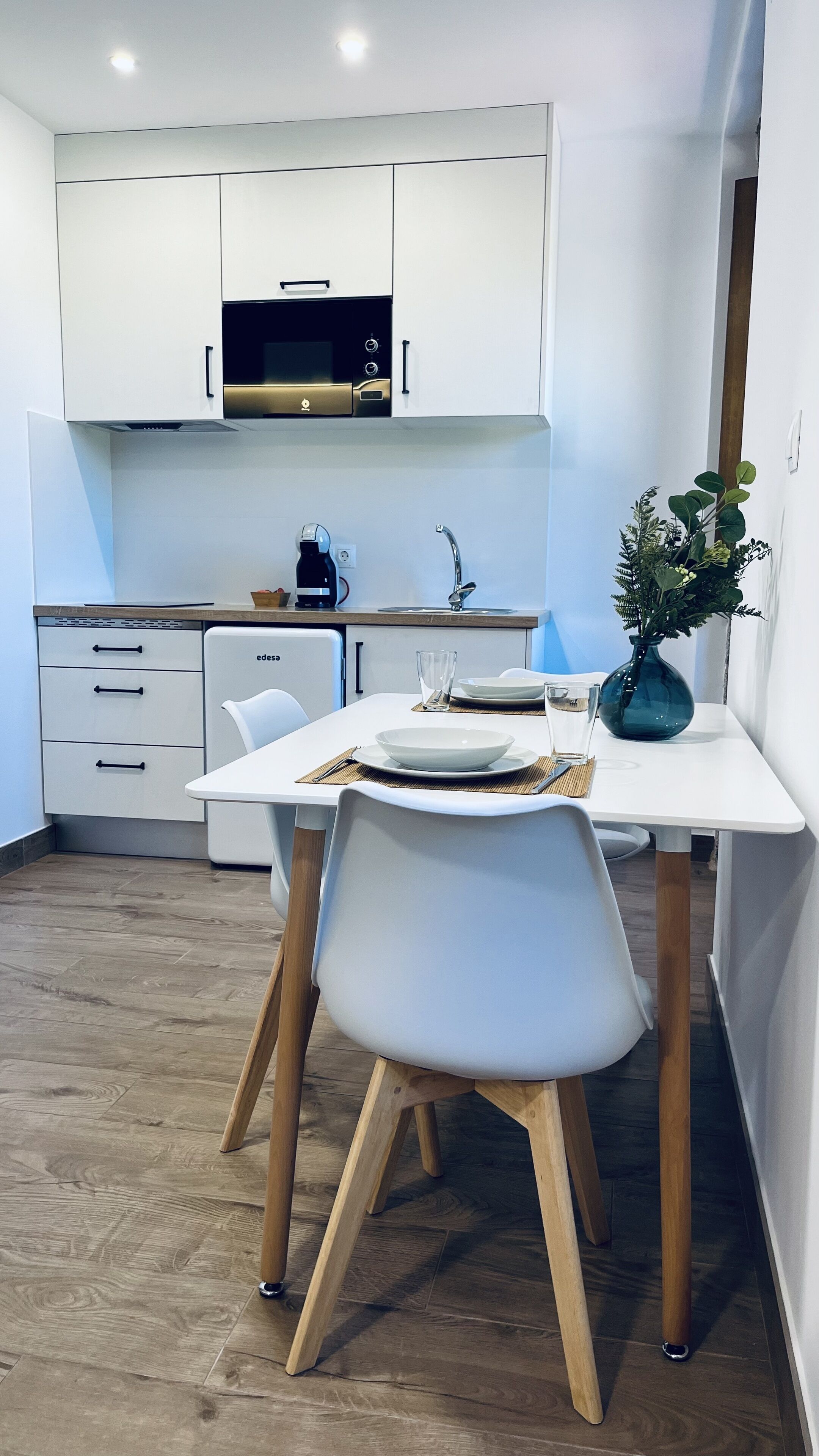 A modern kitchen with white cabinets, a built-in oven, and a dining area with a white table and chairs.