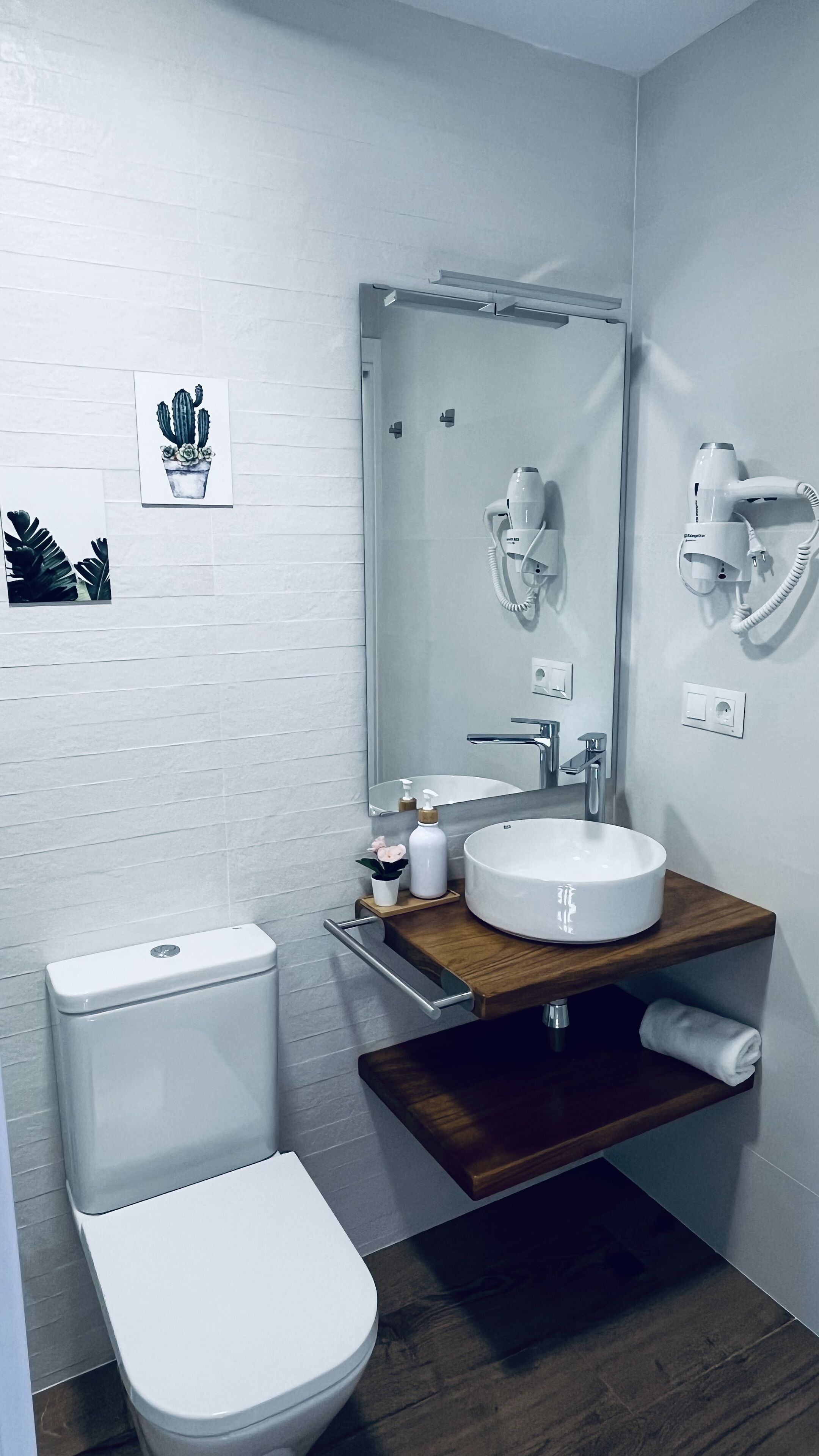Un baño moderno con inodoro blanco, tocador de madera con lavabo y espejo sobre el tocador.