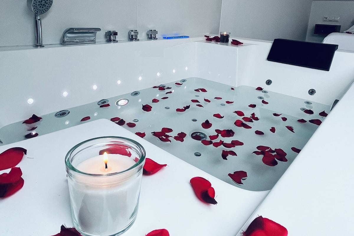A modern bathroom with a bathtub, a glass candle, and rose petals on the floor.